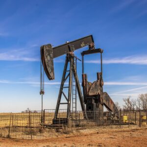 Abandoned rusty oil well pump jack surrounded by cattle fence