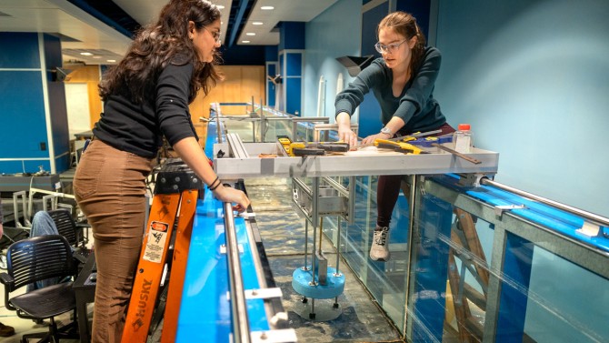 Kavya Mittha ’26, left, and Aisha Brundan ’25 prepare to submerge and test their bobbing buoy wave energy converter at the DeFrees Hydraulics Lab in Hollister Hall.