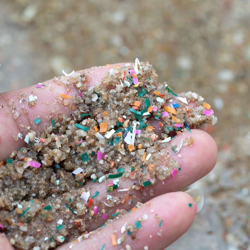Close-up of hand holding seaside sand contaminated with microplastic waste
