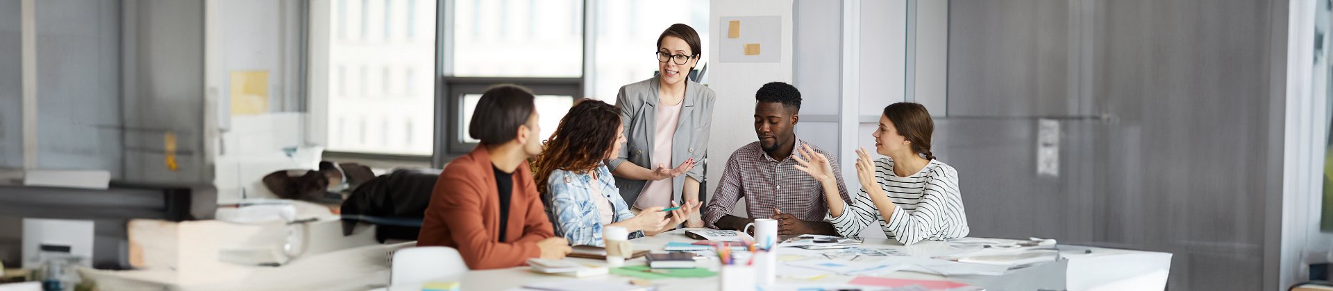 Diverse group of young business people discussing project sitting at table in modern office, focus on female leading