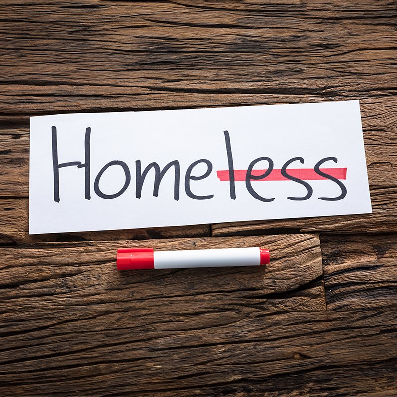 Image of homeless text on paper with strikehthrough on "less" by red marker on wood background