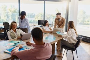 Office professionals collaborate at table with laptops and printed diagrams