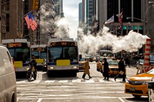 Construction exhaust floating across busy Manhattan street, with buses and taxis